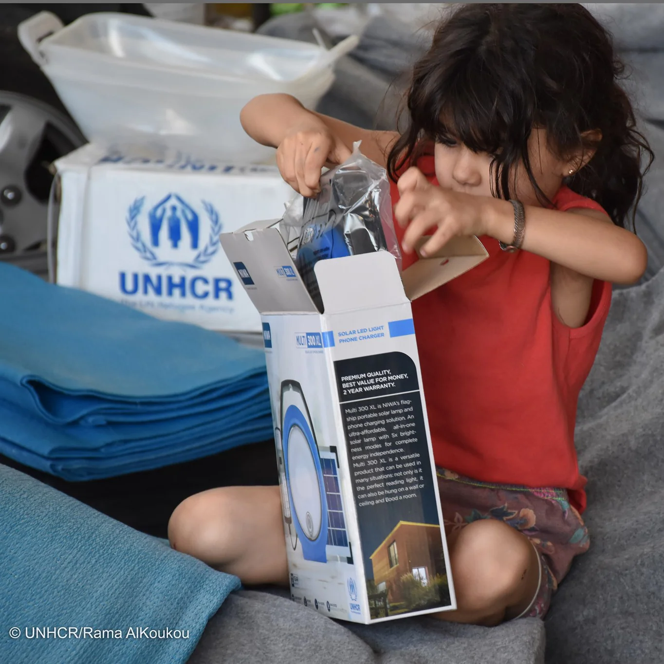 A child using a portable solar light in a setting with UNHCR-branded equipment