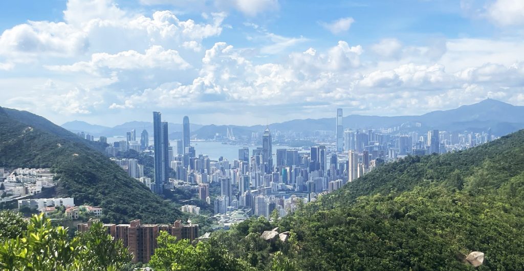 Hong Kong skyline and Victoria Harbour between green hills under a blue sky