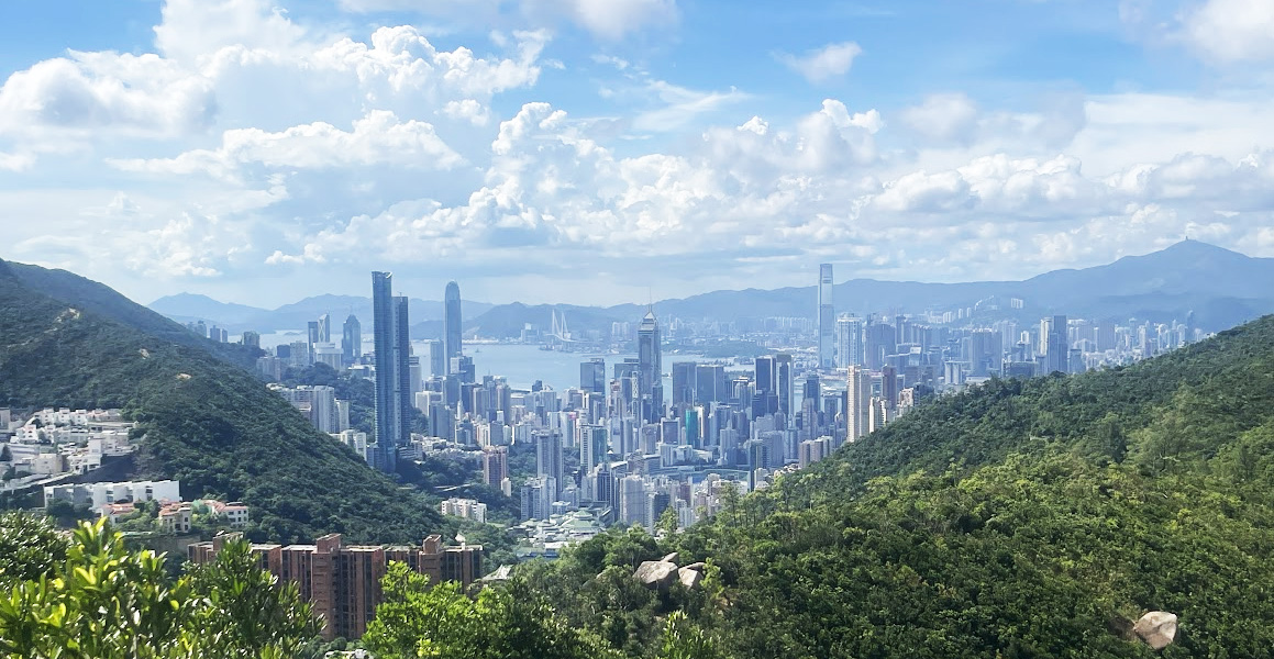 Hong Kong skyline and Victoria Harbour between green hills under a blue sky